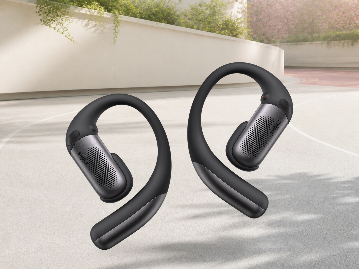 Official black Shokz OpenFit Pro open-ear earbuds shown complete on a warm mineral background