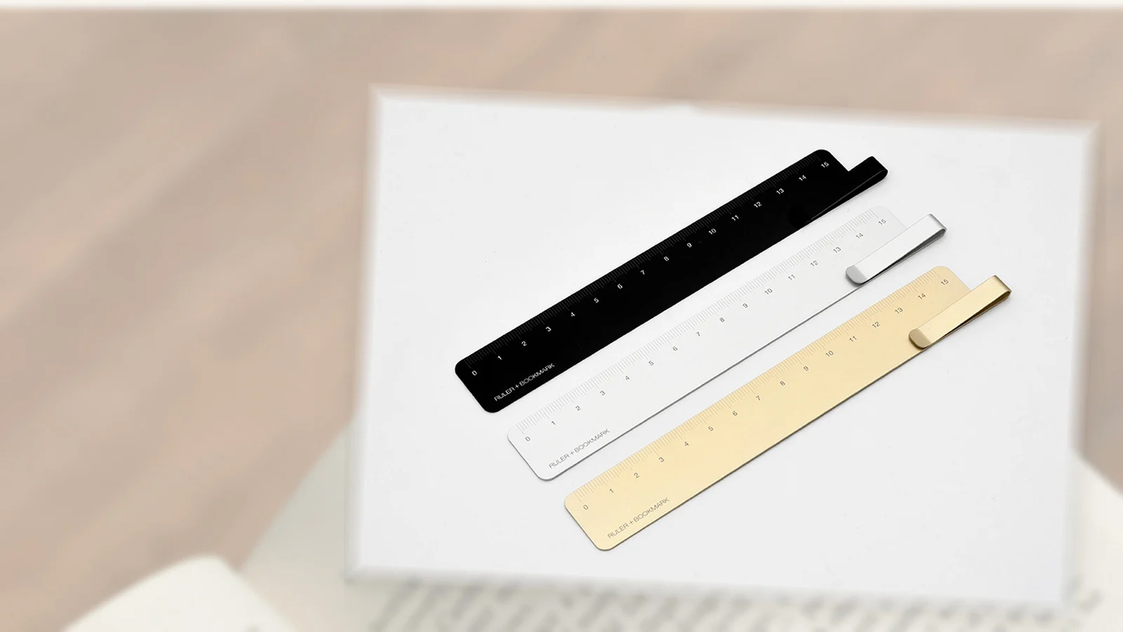 Black, silver and gold KACO RUMA aluminium ruler bookmarks presented over a softly framed reading context